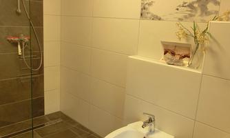 A modern bathroom with a shower and clean, minimalist design. The walls are in neutral tones and there are some decorative elements.