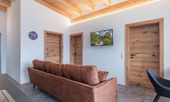 A modern living room with a brown sofa and a television on the wall. Woodwork and two doors give the room a cozy atmosphere.
