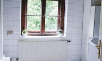 A bright kitchen with white tiles and a large window. The room design is simple and modern, with a view of greenery.