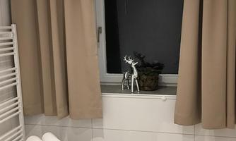 A modern bathroom with a window framed by beige curtains. Decorative items are on the windowsill, and fresh towels are neatly stacked.
