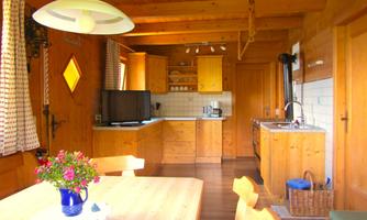 A cozy wooden slatted kitchen with a large table and floral decorations. The kitchen is bright and inviting, with modern accessories.