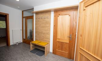 A bright hallway with a wooden bench and wooden paneling. On the right side is a closed wooden door.