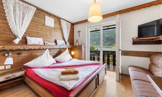 A cozy bedroom with wood paneling and a large bed. Through the open doors, there is a view of the surrounding mountains.