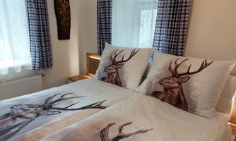 A cozy bedroom with a double bed and bedding that features a deer print. Bright curtains and stylish wall decor complement the space.