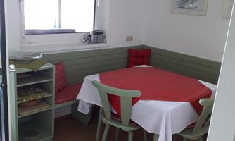 A cozy dining area with a red table and white chairs. The wall is designed in gentle shades of green and white, with a window for plenty of natural light.