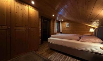A cozy bedroom with wood paneling and a double bed. The soft lighting and the carpet create a warm atmosphere.