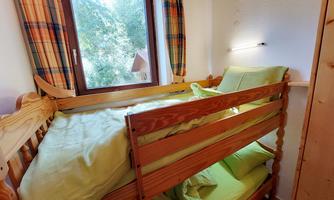 A cozy room with a loft bed and light green bedding. A window lets in plenty of daylight and offers a view of the outdoors.
