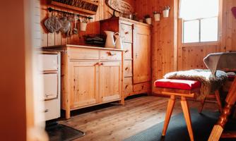 A cozy wooden kitchen with a stove, a table, and chairs. Plenty of natural light streams through the window.