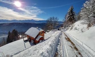 A snowy landscape with an orange house and blue sky. The path is clearly cleared and the mountains are visible in the background.