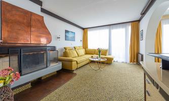 A cozy living space with a yellow sofa and a fireplace. Large windows let in plenty of light, and the rug has an interesting pattern.