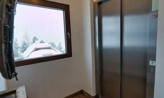 An elevator in a modern building with a window overlooking a snowy landscape. The floor is made of wood and conveys a cozy atmosphere.