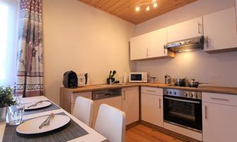 A modern kitchen with wooden shelves and white cabinets. On the table are set plates and a glass.