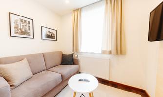 A cozy living room with a gray sofa and a round table. Pictures hang on the walls, and there are bright curtains that let light in.