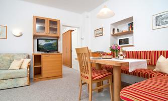 A cozy living room with a dining table and a couch. There are wooden shelves and a TV in the room.