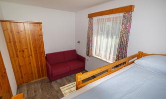 A cozy bedroom with a bed and a red sofa. Large windows let in plenty of daylight.