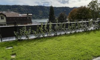 A beautiful garden with green grass and a view of a lake. In the background, trees and hills are visible.