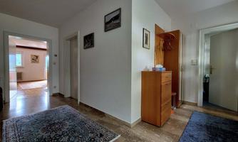 A bright hallway with white walls and a wooden cabinet. Two rugs are on the floor and there are various doors leading to other rooms.