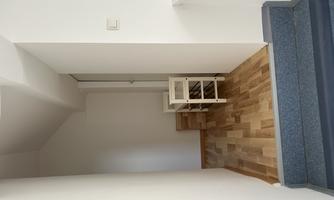 A bright hallway with wooden flooring and white walls. At the end of the hallway are two small pieces of furniture.