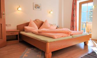 A cozy bedroom with a large bed and soft, pink pillows. Next to the bed is a nightstand, and there is access to a balcony with a view.