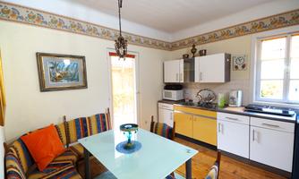 A bright kitchen with a modern table and colorful cushions. The windows let in plenty of daylight, and the furnishings are functional.