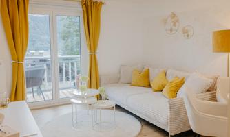 A bright living room with a comfortable sofa and yellow cushions. The large windows provide a beautiful view and ensure plenty of daylight.