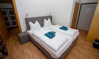 A simple, bright room with a double bed and fresh towels. The wooden floors and neutral color scheme create a relaxed atmosphere.