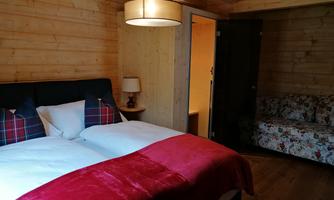 A cozy bedroom with a double bed and red accents. The room features a rustic wooden ceiling and a seating area with a floral sofa.