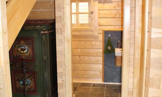 A cozy hallway with wooden walls and a modern tiled floor. On the left side, there is a decorative wood stove, and in the background, a room with an open door is visible.