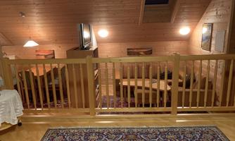 A cozy living room in a wooden house. There is a seating area, a television, and a beautiful carpet.