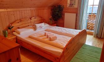 A cozy bedroom with wood paneling and a large double bed. The room is bright and inviting, featuring a carpet and windows that let in natural light.