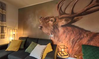 A cozy living space with a sofa, colorful cushions, and a large mural of a majestic deer. The atmosphere is complemented by soft light and stylish decor.