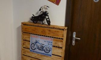 A decorative wooden cabinet stands in a corner with a model motorcycle and two nostalgic signs on the wall. The door is made of wood and encloses the area.