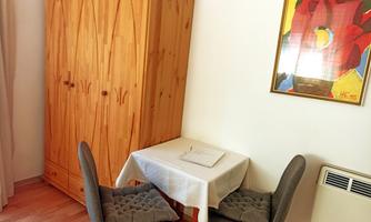 A cozy room with a wooden cupboard and a table with two chairs. A colorful painting hangs on the wall.