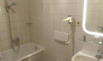 A small bathroom with a bathtub, a shower, and a sink. It has tiled walls and a large mirror.