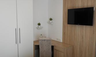 A modern room with a television on the wall and a desk. The room contains plants and a wardrobe made of light wood.