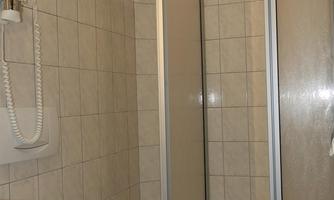 A simple bathroom with a shower cubicle and a sink. The walls are tiled and bright.
