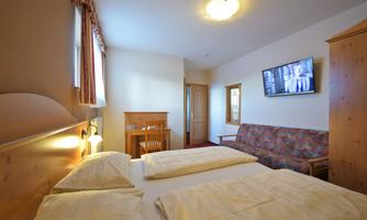 A simple hotel room with two beds, a television, and a small living area. The room is bright and comfortably furnished.