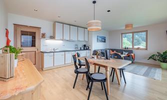 A bright, modern kitchen with a dining area. The room is open and inviting, with large windows and wooden details.