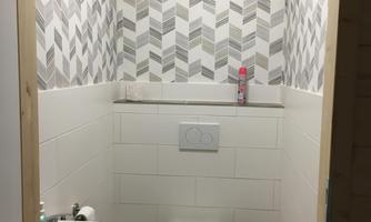 A modern bathroom with an elegant wall design in geometric pattern. It features a toilet and a small sink.