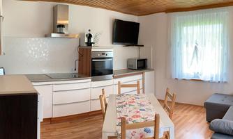 A modern kitchen with a dining table and a cozy seating area. The room is bright and inviting with large windows.