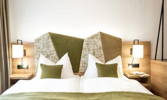 A stylish double room with a modern headboard and cozy pillows. The soft green tones and wood create a relaxing atmosphere.