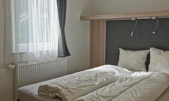 A modern bedroom with a large bed and white bedding. A window with a light curtain lets in natural light.