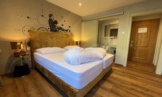 A modern room with a cozy double bed and soft colors. Large windows provide plenty of daylight.