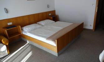 A simple room with a double bed and two nightstands. The walls are light and there is a cozy armchair in the corner.