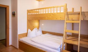 A cozy room with a wooden loft bed. Cozy pillows and blankets lie on the bed.
