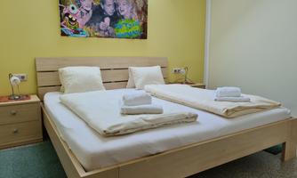 A cozy bedroom with a large double bed and fresh towels. A colorful piece of art with cheerful figures hangs on the wall.