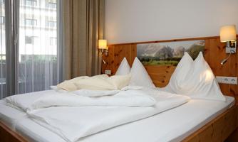 A cozy bedroom with a large bed and white pillows. The wooden paneling and soft lighting create an inviting atmosphere.