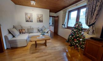 A cozy living room with a comfortable sofa and a small table. In the corner stands a decorated Christmas tree.