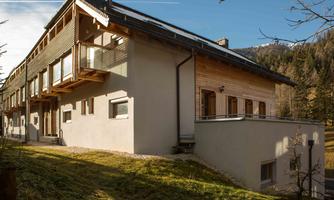 A modern building with wooden cladding and large windows. It is located in a picturesque landscape between mountains.