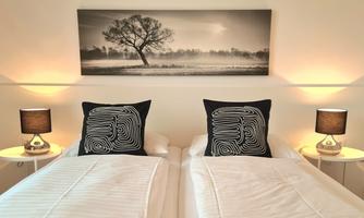 A modern bedroom with two single beds and elegant pillows. A piece of art featuring a tree in black and white hangs on the wall.